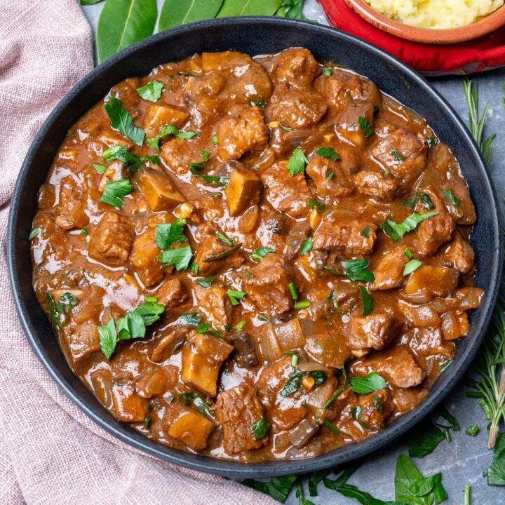 meat and vegetable stew in a skillet on a table next to a bowl of mashed potatoes