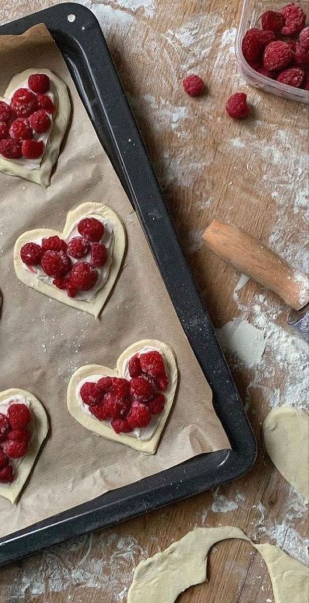 heart shaped cookies are on a baking sheet with raspberries in the shape of hearts