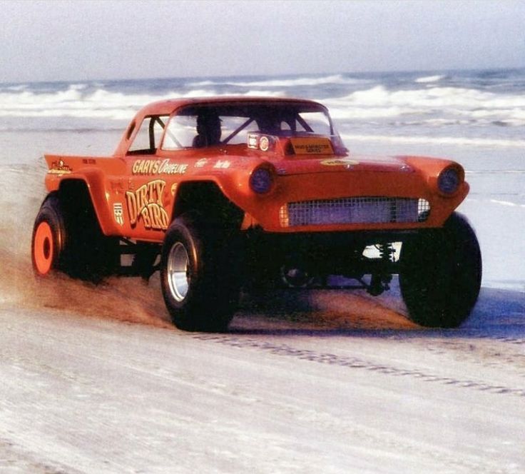 an orange truck driving down a sandy beach