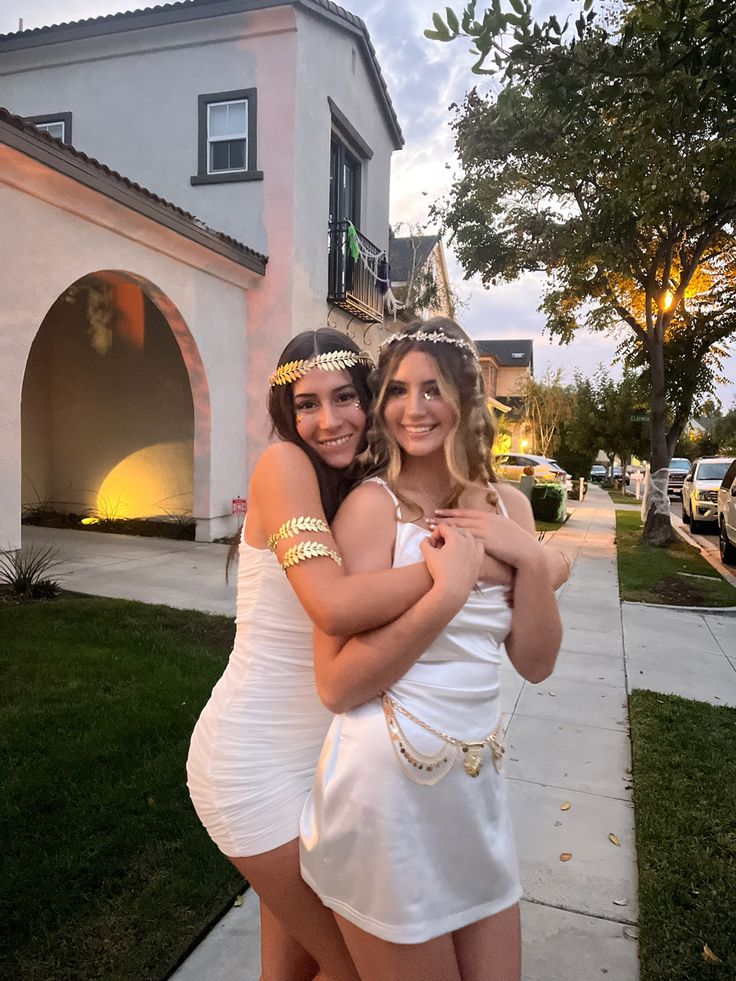 two women in white dresses hugging each other on the sidewalk next to a large house