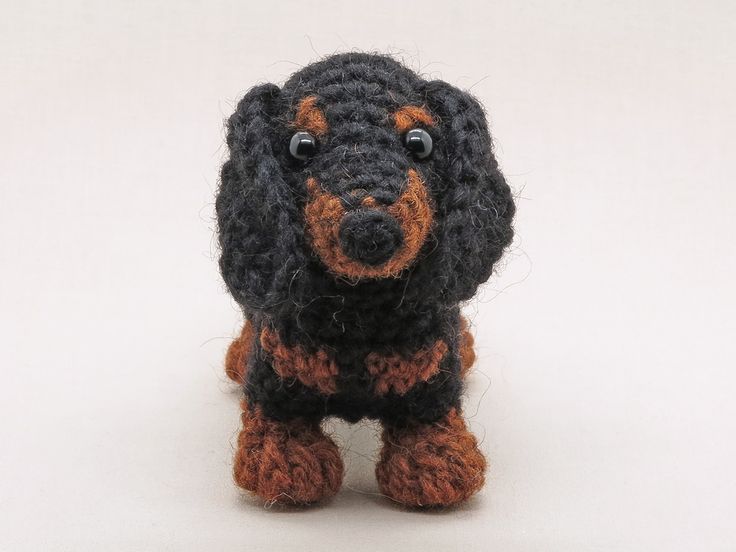 a crocheted black and brown dog sitting on top of a white floor next to a wall