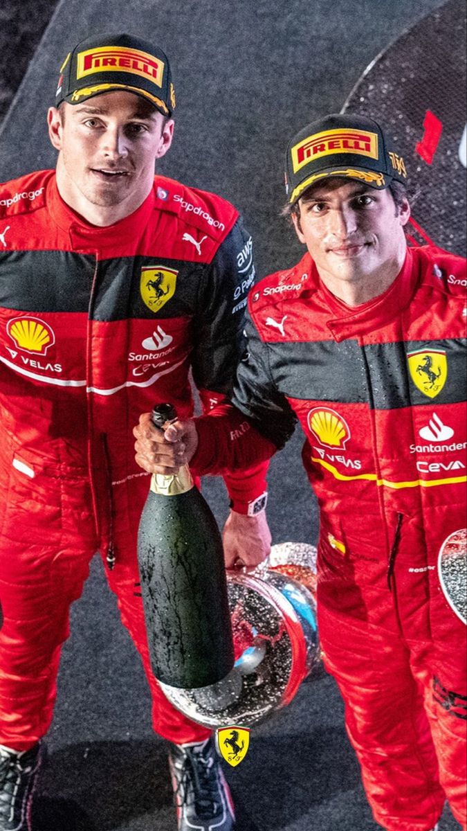 two men in red racing suits holding trophies and champagne bottles with their arms around each other