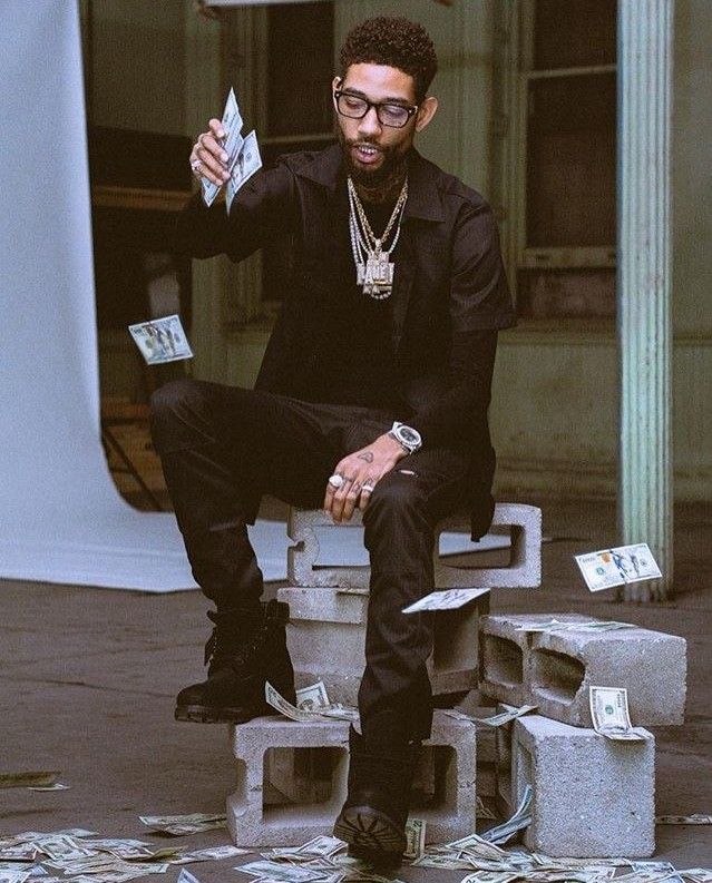 a man sitting on top of a cement block holding money in his hand and wearing glasses