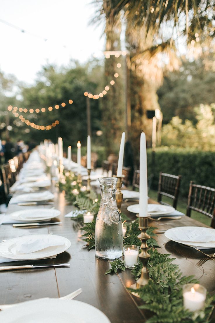 a long table is set up with candles and place settings for an outdoor dinner party