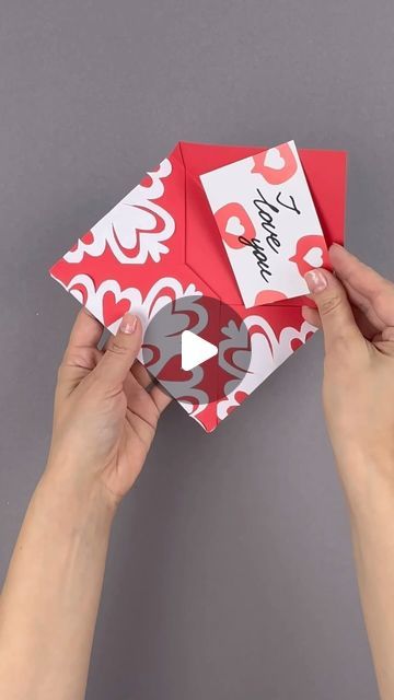 two hands are holding an origami box with hearts and the word happy valentine's day written on it