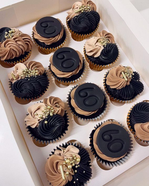 twelve decorated cupcakes in a white box with black frosting and gold decorations