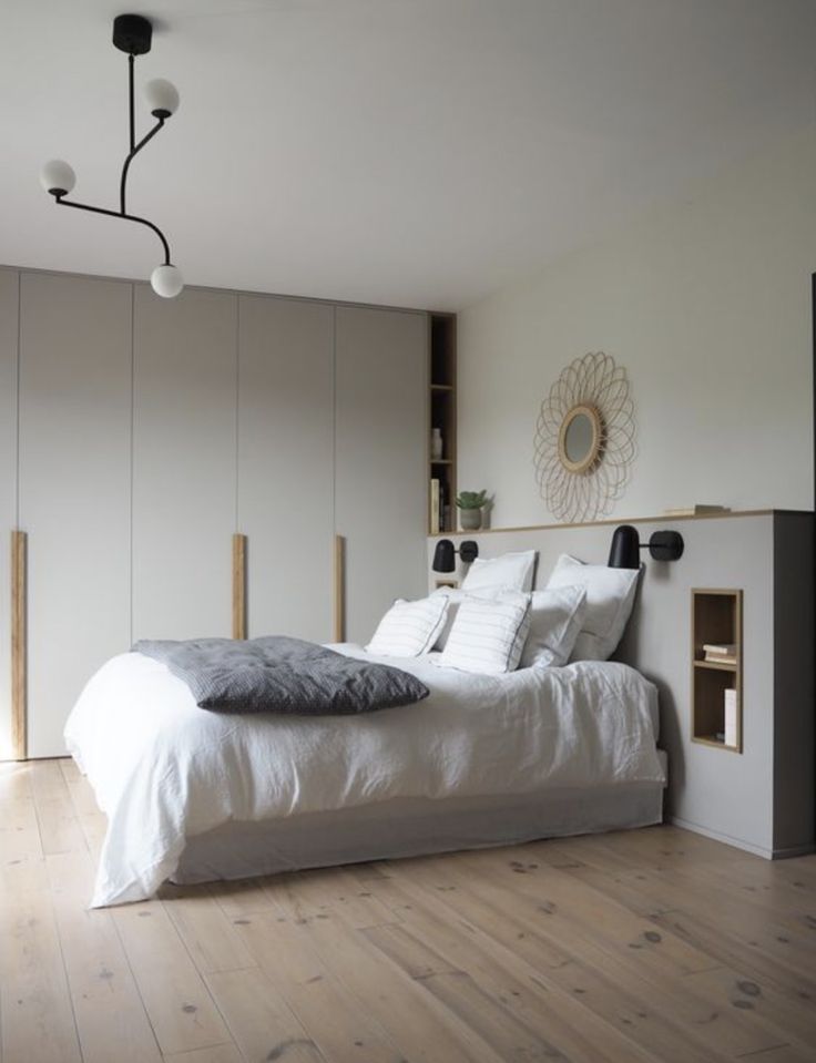 a white bed sitting on top of a wooden floor next to a wall mounted book shelf