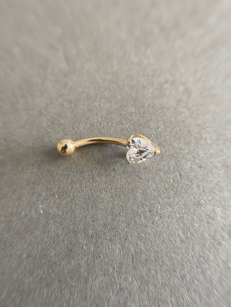 a gold nose ring with a single diamond on the top, sitting on a gray surface