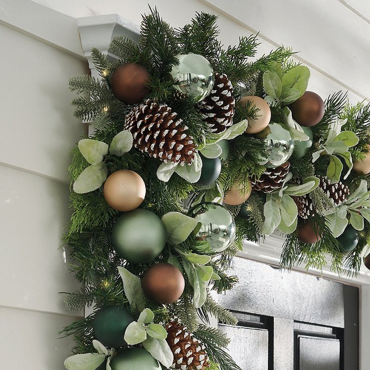 a christmas wreath with pine cones and evergreen leaves hanging from the front of a house