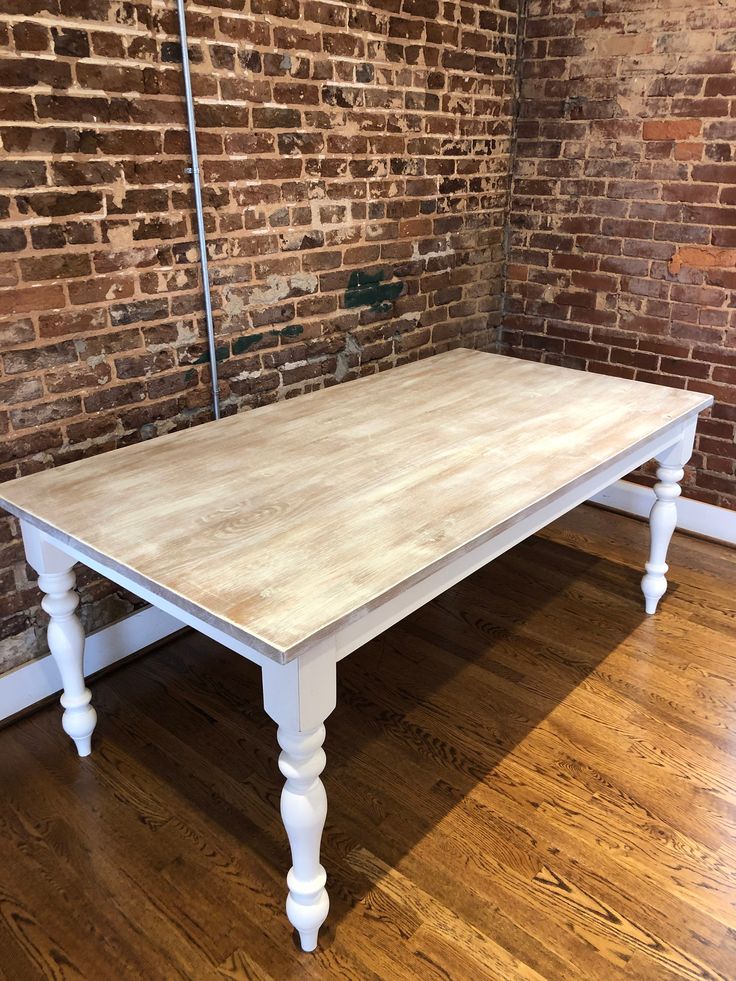 a white table sitting on top of a hard wood floor next to a brick wall