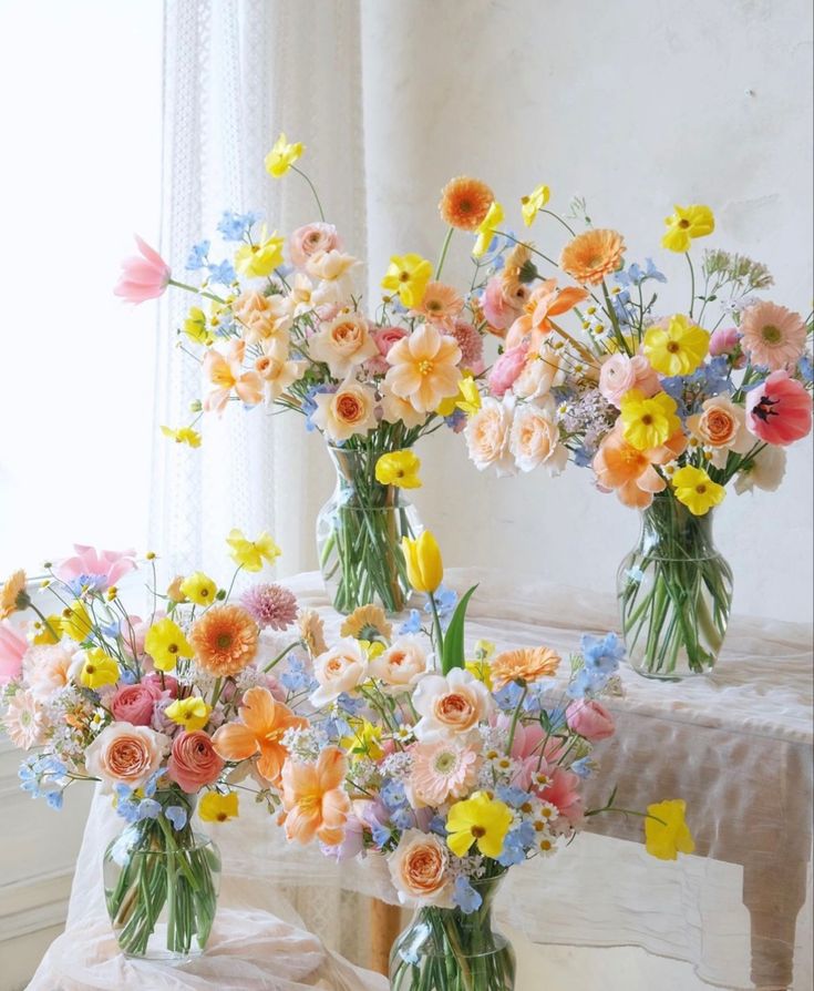 two vases filled with colorful flowers sitting on a table next to a white table cloth