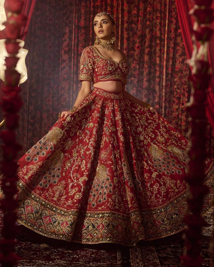 a woman in a red and gold bridal gown standing next to a red curtain