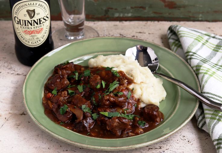 a green plate topped with meat and mashed potatoes next to a bottle of guinness