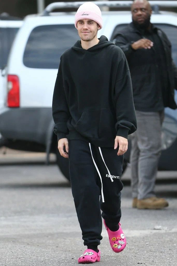 a man wearing pink shoes and a black hoodie is walking down the street with another man in the background