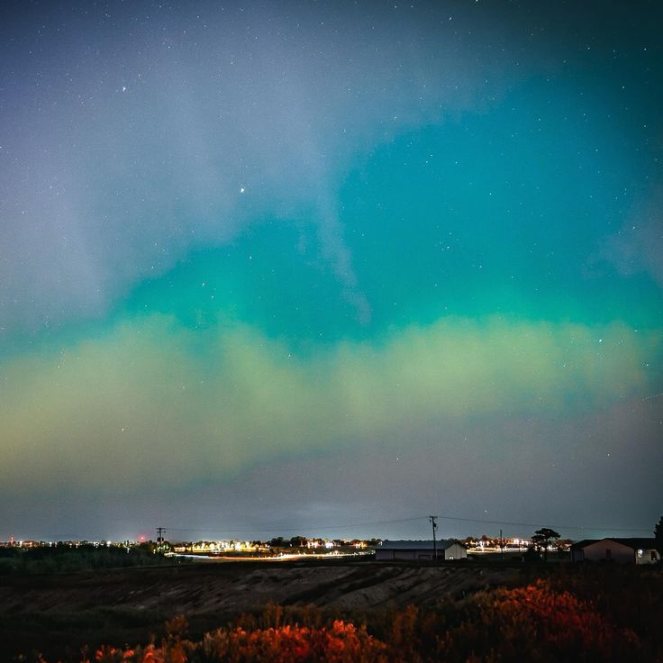 an aurora bore is seen in the sky above a field with trees and buildings at night