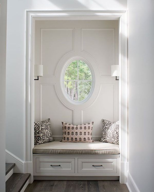 a window seat in the entry way of a house with white walls and wood flooring