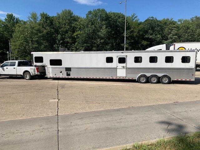 a horse trailer parked in a parking lot next to a white truck and some trees