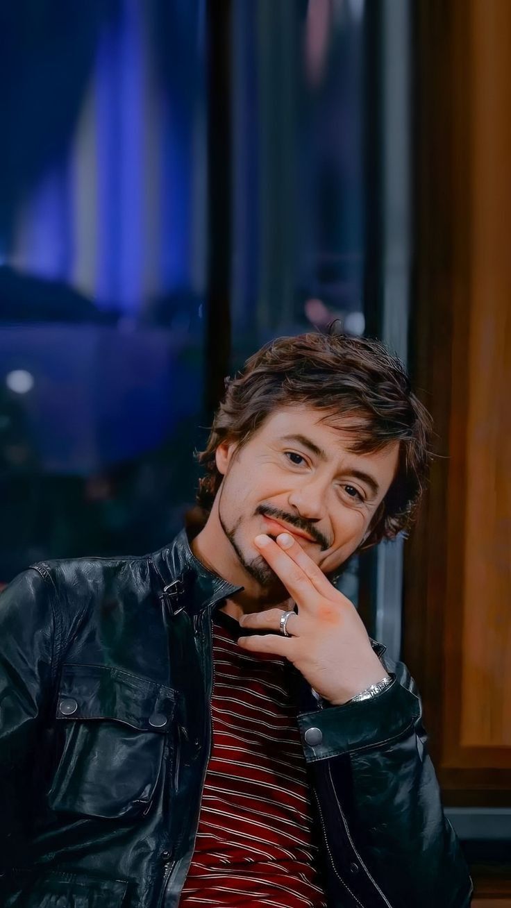 a man with a moustache on his face sitting in front of a window