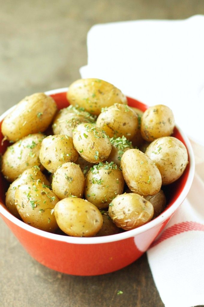 a red bowl filled with potatoes on top of a wooden table next to a napkin