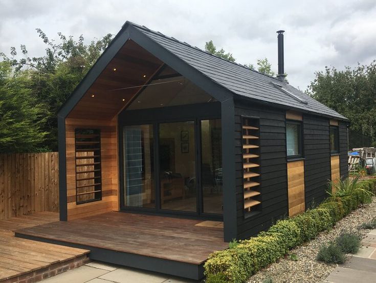 a small black cabin with wooden decking and windows