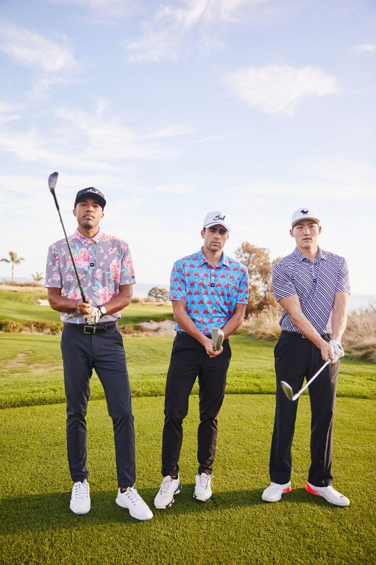 three men standing next to each other on top of a green golf field holding golf clubs