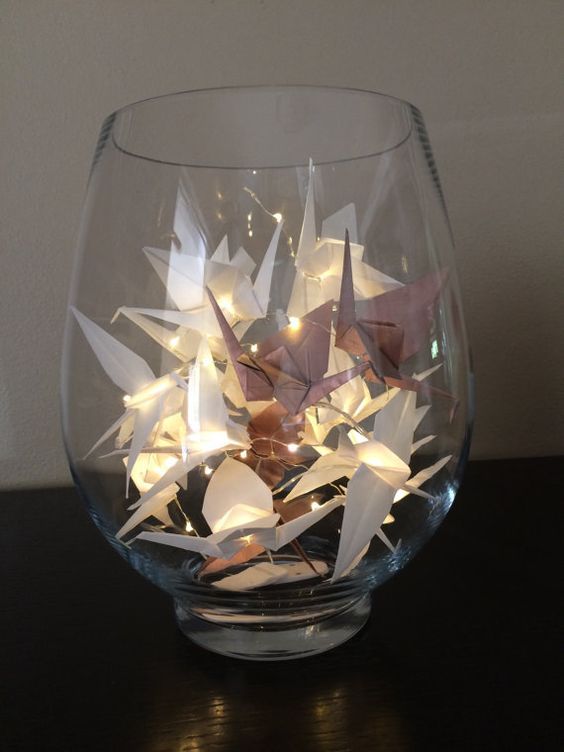 a glass filled with paper cranes on top of a table