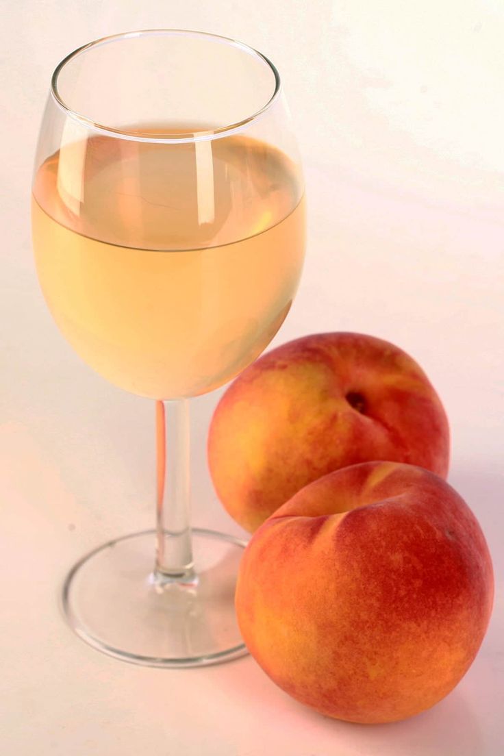 two peaches next to a glass of white wine