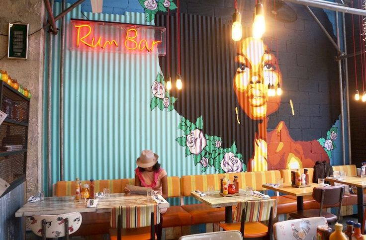 a woman sitting at a table in front of a wall with a painting on it