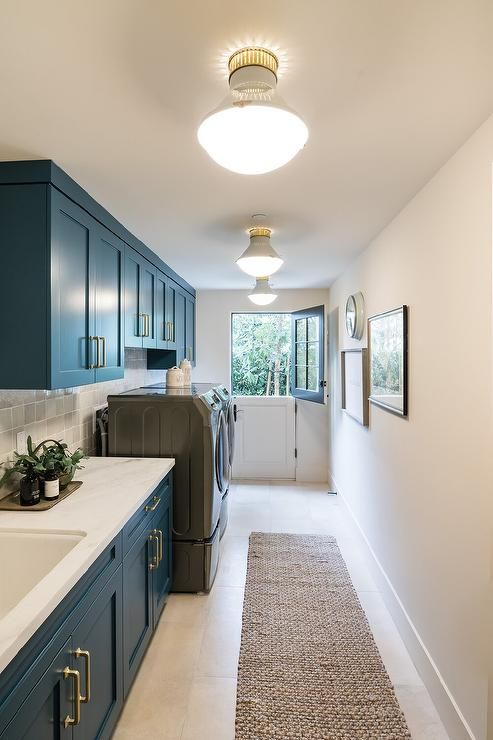 a long hallway with blue cabinets and white counter tops, along with a washer and dryer