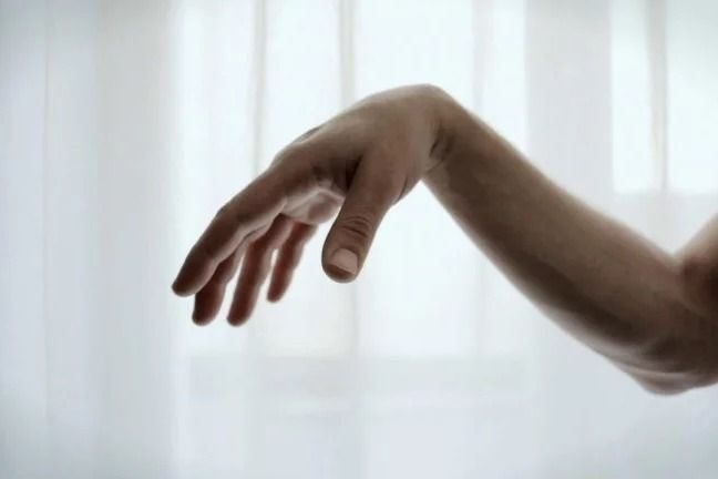 a person's hand reaching for something in front of a window with sheer curtains