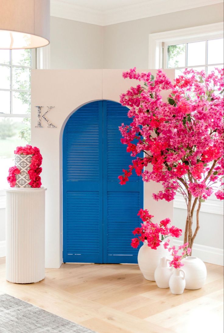 pink flowers are in vases next to a blue door and white vase with red flowers