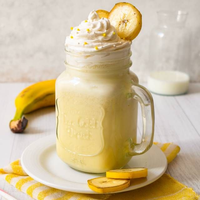 a banana smoothie in a mason jar with whipped cream and sliced bananas on the side