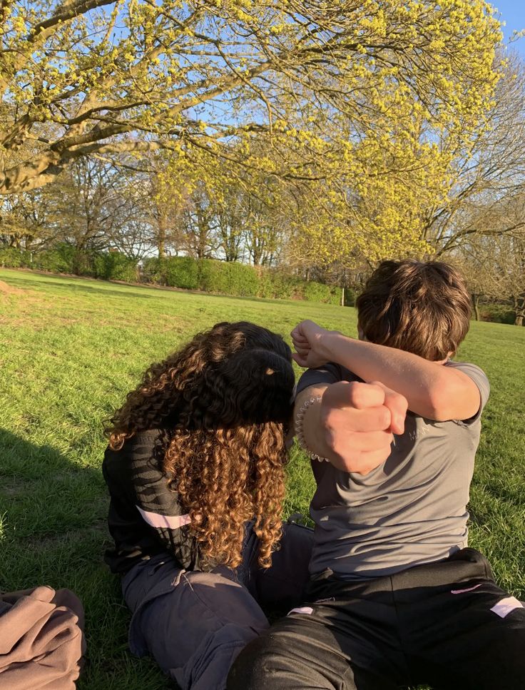 two people sitting in the grass with their arms around each other