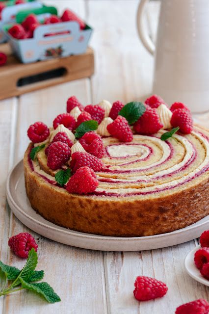 a cake with raspberries and cream frosting on a plate next to some berries