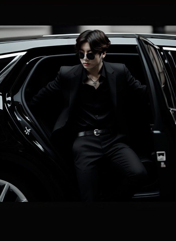 a man sitting in the back of a car wearing sunglasses and a black suit with his hands on his hips