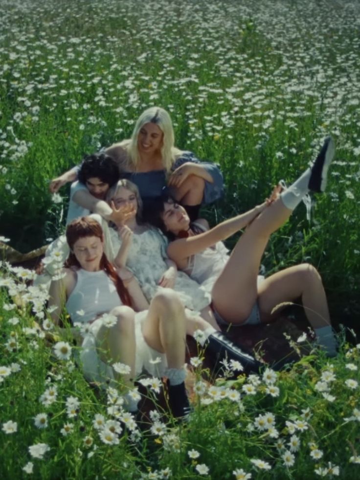 a group of young women sitting on top of a lush green field filled with white flowers