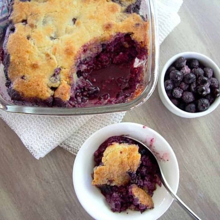 blueberry cobbler in a glass dish next to two bowls of berries