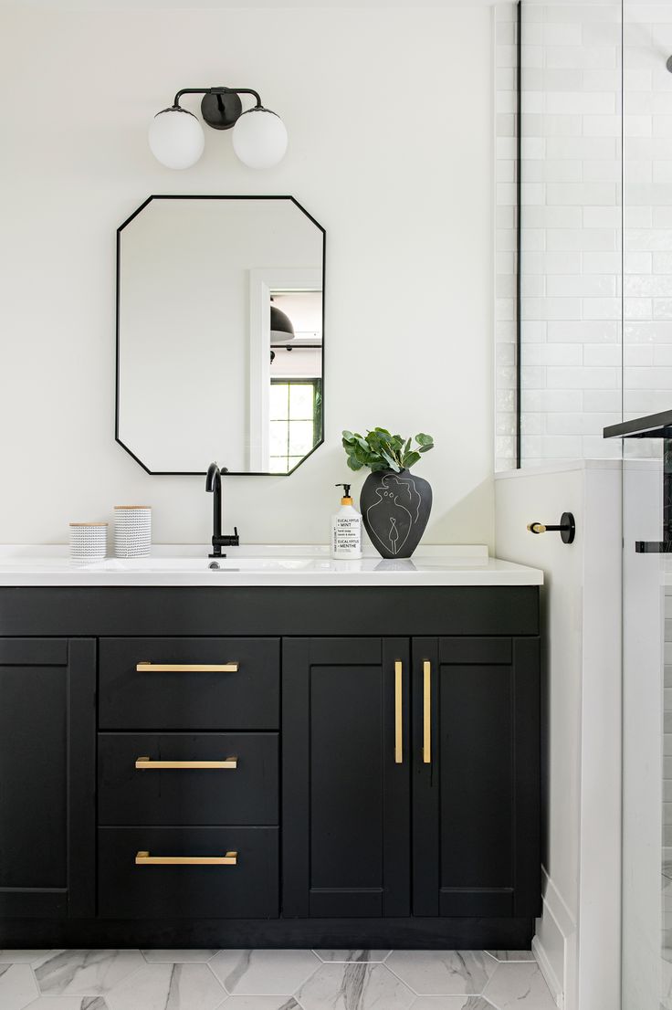 a black and white bathroom with gold handles on the vanity, mirror over the sink