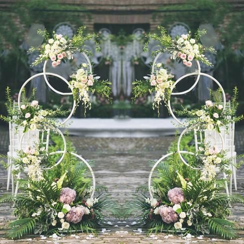 two metal archways with flowers and greenery in front of an outdoor wedding ceremony