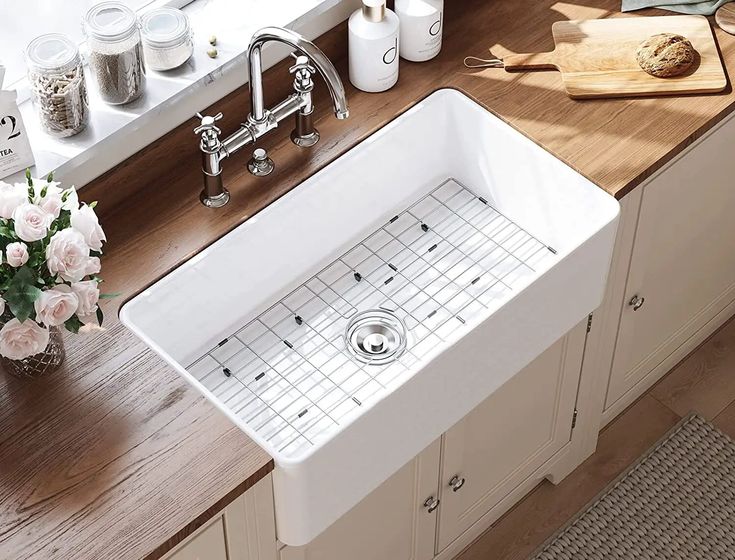 a white kitchen sink sitting on top of a counter next to a cutting board and flowers