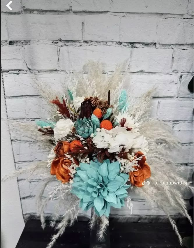 a vase filled with flowers and feathers on top of a wooden table next to a brick wall