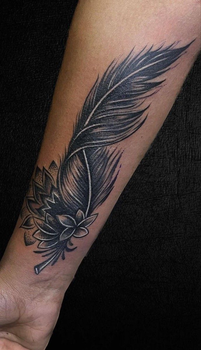 a black and grey feather tattoo on the left arm with an ink pen in it