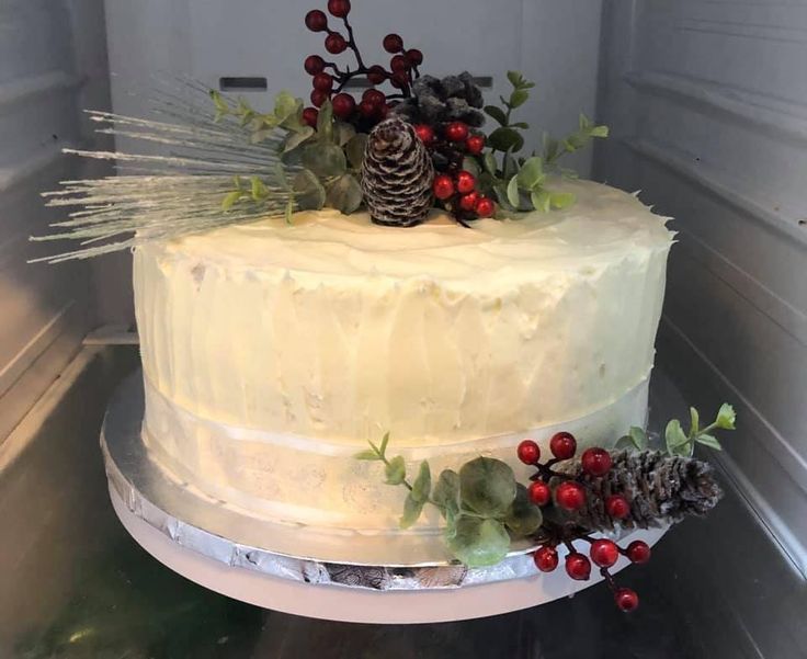 a white frosted cake decorated with berries and pine cones