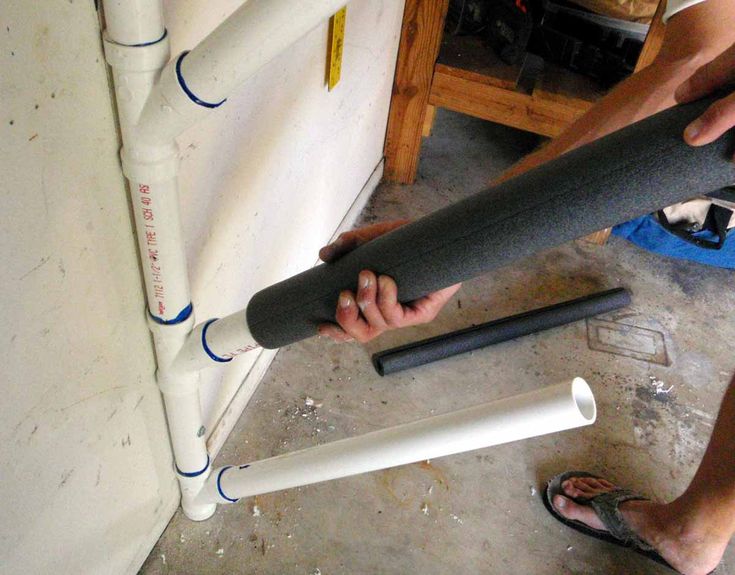 a man standing next to a large pipe on top of a cement floor in front of a white wall