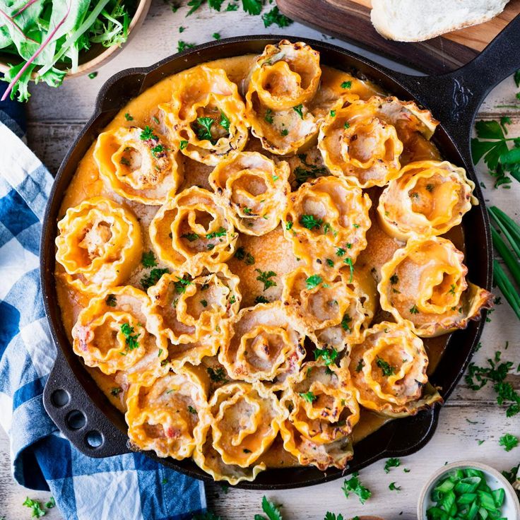 a skillet filled with pasta and meat on top of a wooden table next to bread