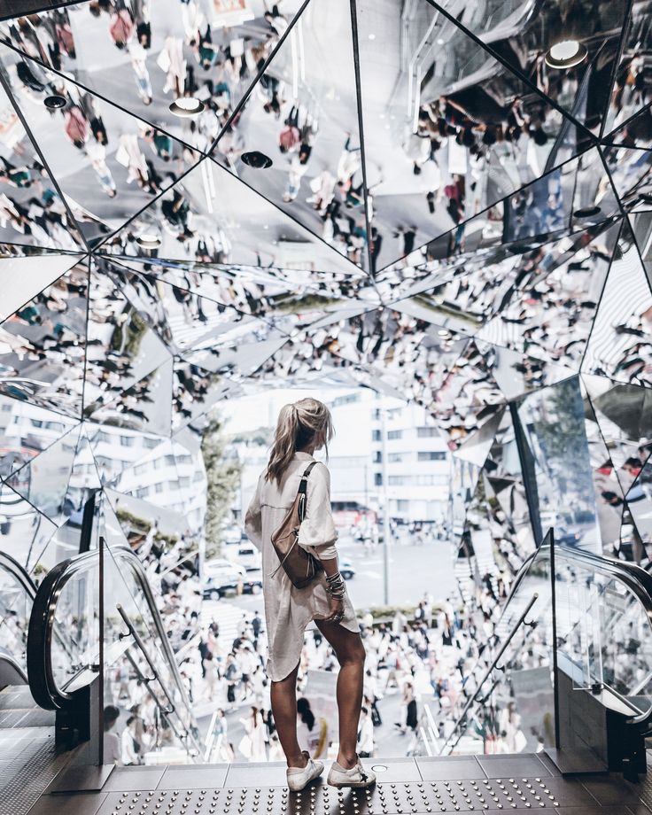 a woman is standing on an escalator in front of many mirrors and people