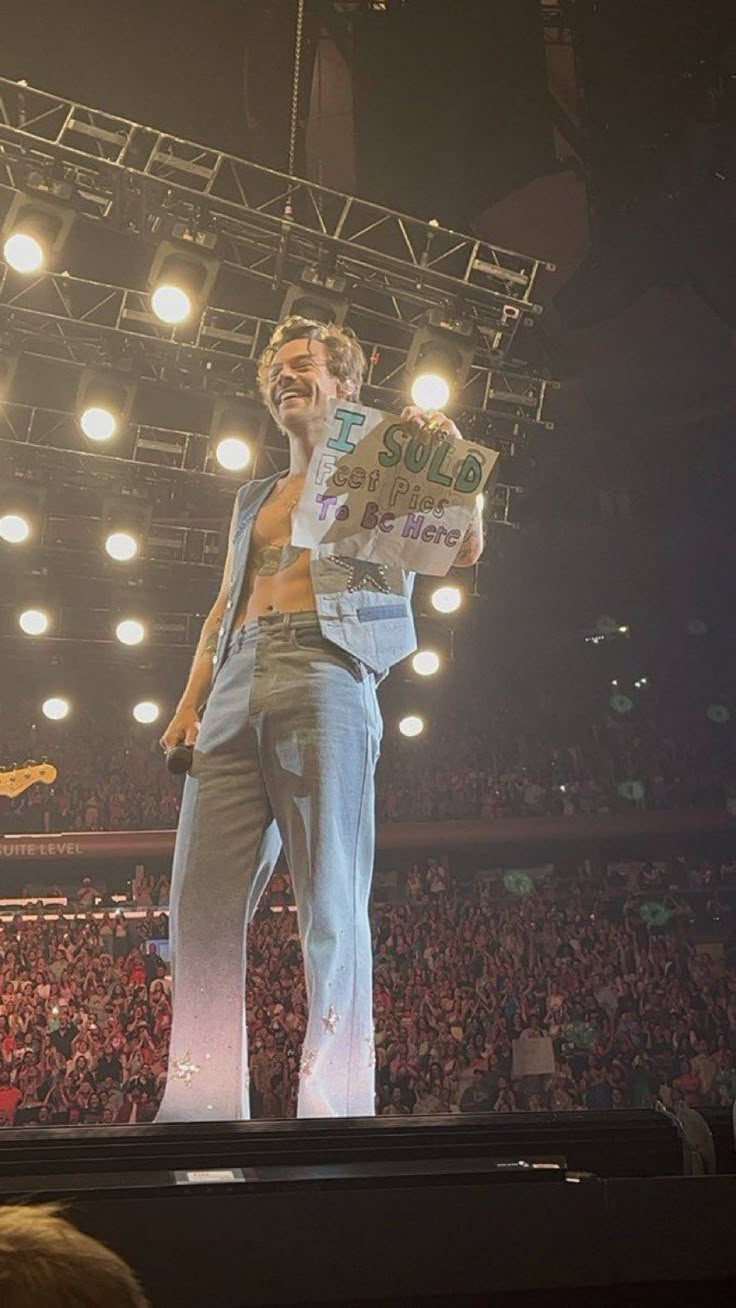 a man standing on top of a stage in front of a crowd holding a sign