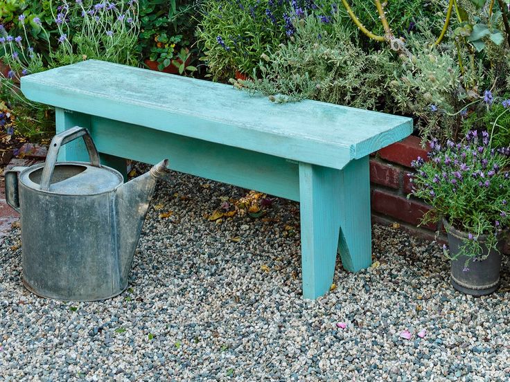 a blue bench sitting next to some potted plants and a bucket on the ground