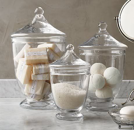 three glass containers filled with different types of bath items on a counter top next to a mirror