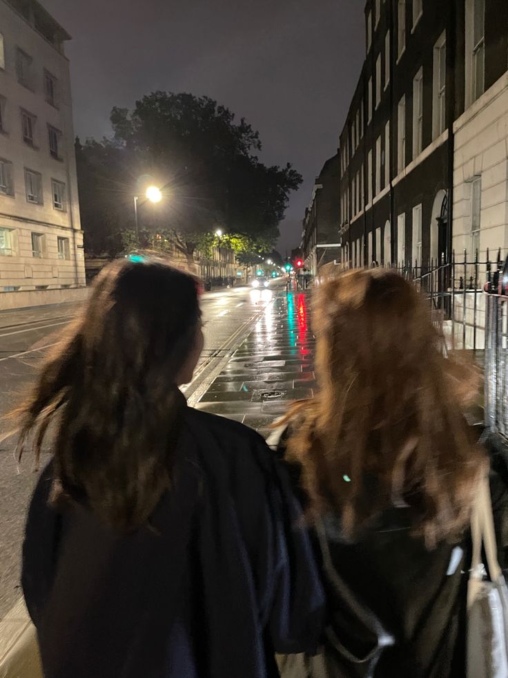 two women walking down the street at night with their backs turned to the camera,